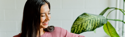 Smiling woman with a cup, sitting on a sofa next to plant